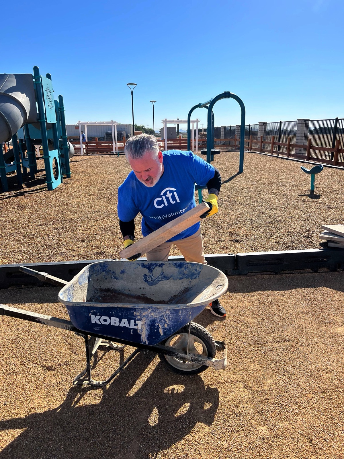 Travis Avery volunteering at a playground build, loading lumber into a wheelbarrow